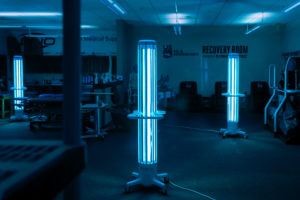 Three Arc disinfection devices glowing and standing apart in a dark room.